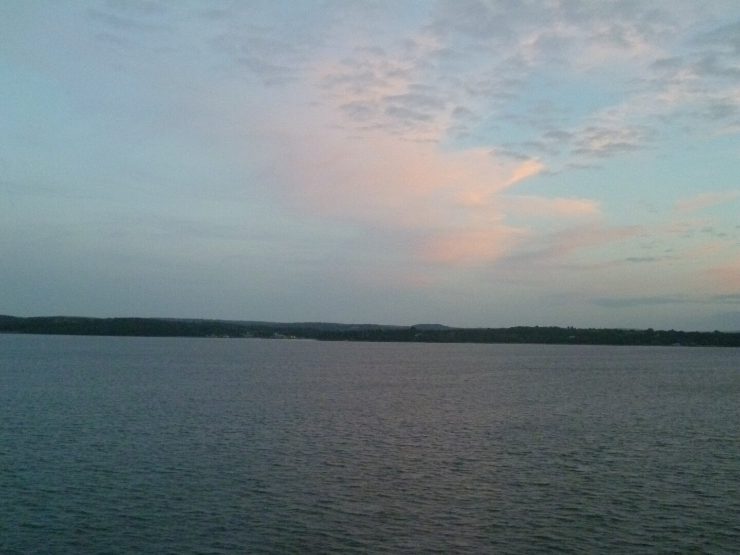 A pink cloud in a blue sky, reflected in the dark water of the Channel below.